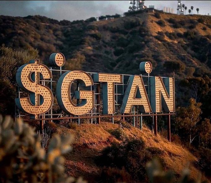 An illuminated "SCGTAN" sign sits on a hillside reminiscent of the Hollywood sign.