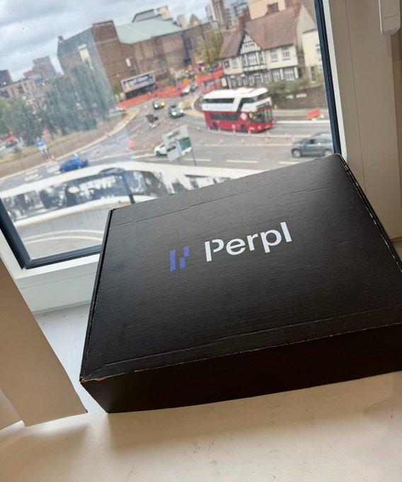 A black cardboard box with the 'Perpl' logo (a stylized purple 'P' and white text) sitting on a white windowsill, with a view of a London street featuring a red double-decker bus and traditional architecture through the window.
