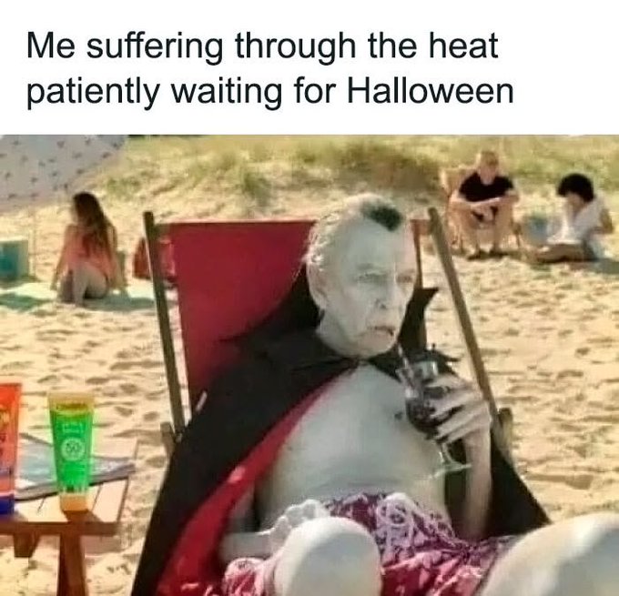 A meme image showing a pale, bald figure in a black cape relaxing in a beach chair holding a goblet, with text reading 'Me suffering through the heat patiently waiting for Halloween'.