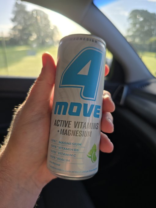 A hand holding a '4 MOVE Active Vitamins + Magnesium' beverage can inside a car, showing 50% Magnesium, 100% Vitamin B6, 100% Vitamin C, and 100% Niacin on the label.