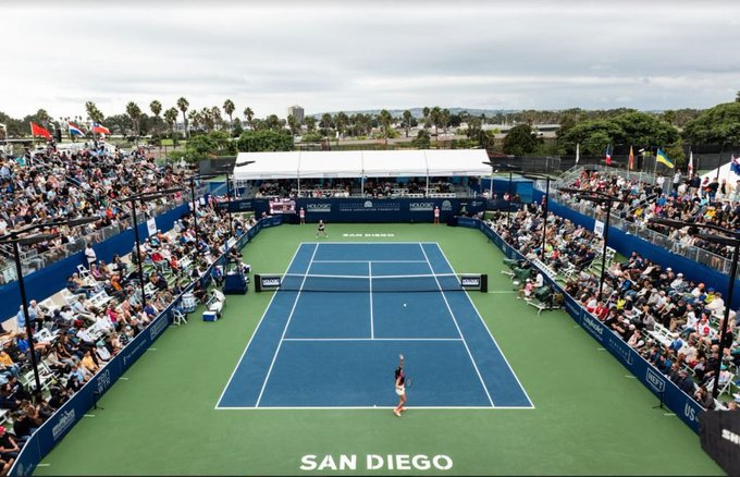 An aerial view of a tennis match in San Diego, with players on a blue court and spectators filling the stands.