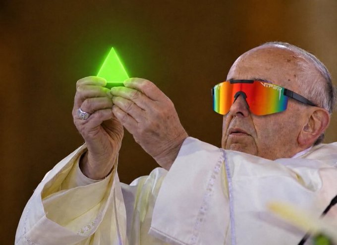 Pope Francis wearing large Oakley sunglasses with mirrored lenses, holding up a small, glowing green object.