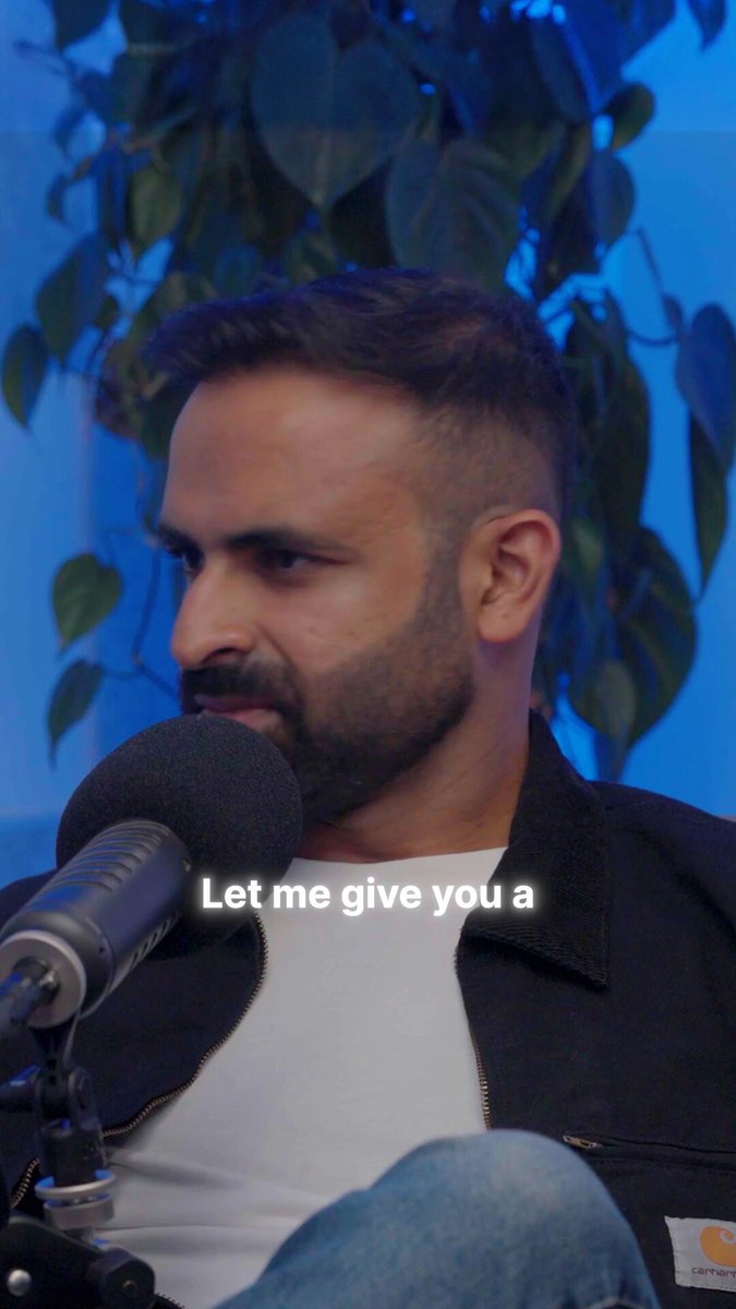 The image shows a man sitting at a microphone, wearing a black jacket with white text on his chest. The caption reads "Let me give you a tokenisation" which suggests that the man might be discussing the concept of tokenisation or its implementation in the context of the image.