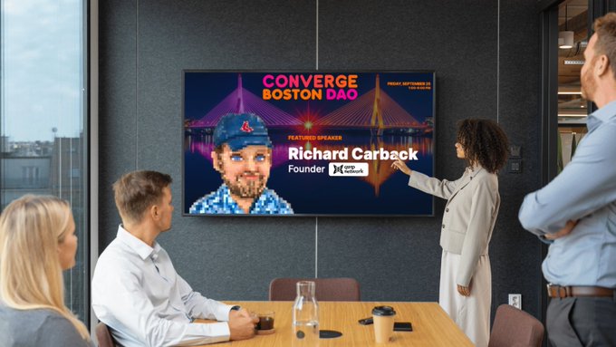 A business meeting scene where colleagues view a screen displaying "CONVERGE BOSTON DAO" with featured speaker "Richard Carback, Founder" at the top of the image.