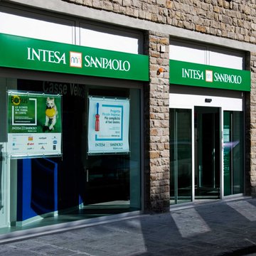 The image shows the exterior of an Intesa Sanpaolo bank branch, displaying the prominent green signage with the bank's name and logo. The caption reads: "The storefront of an Intesa Sanpaolo branch, Italy's largest bank, which has dramatically reduced its BlackRock Bitcoin ETF holdings by 94% while tripling its position in the BlackRock Staked Ethereum ETF."