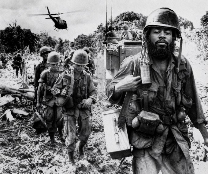 A group of exhausted, bearded soldiers in helmets march in single file through a muddy jungle trail, with a helicopter hovering overhead and additional troops visible in the background.

The accompanying post references a Solana giveaway contest with an 8-hour deadline, using the war imagery likely to evoke themes of perseverance or "battle" in a meme-like fashion—a contrast between serious historical combat and casual crypto promotion.