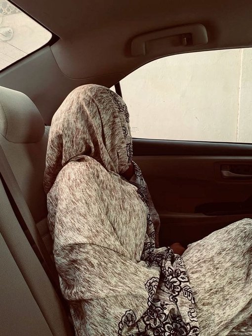 A person wearing a patterned gray hijab and matching outfit sleeps in the passenger seat of a car.