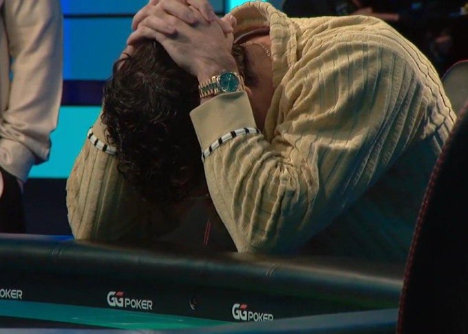 A man wearing a cream cable-knit sweater sits at a poker table with his head in his hands in apparent frustration or exhaustion, with 'GG Poker' visible on the table's edge.