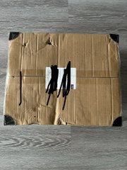 A cardboard shipping package with black handwritten markings rests on a gray wooden surface.