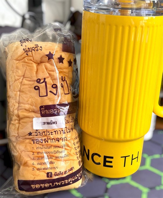 A packaged loaf of Thai sandwich bread with Thai text, sitting next to a yellow tumbler with the partial text "NCE TH" visible.