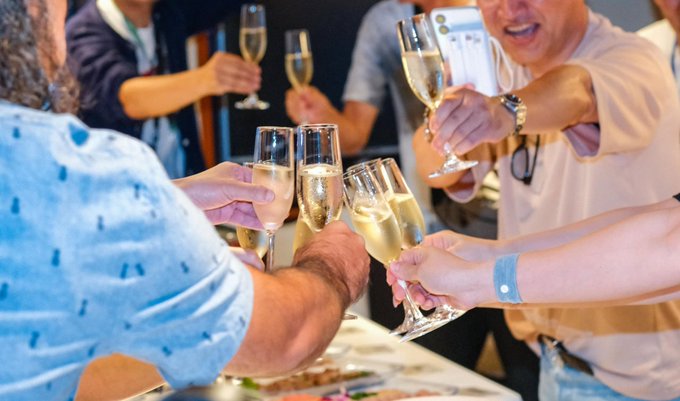A group of people raise champagne flutes in a celebratory toast, with their hands and glasses clustered in the center of the frame.