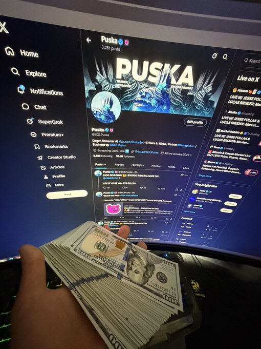 A hand holds a stack of U.S. hundred-dollar bills in front of a computer screen displaying the Twitter/X profile of "Puska" (@OLPuska) with 3,261 posts.