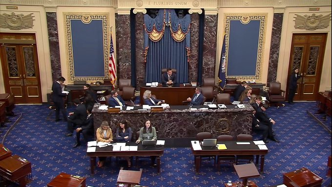Members of the U.S. Senate gather in the ornate Capitol chamber, with the motto "E PLURIBUS UNUM" displayed prominently above the draped American flags, preparing for the upcoming vote on the CLARITY Act. Staffers and senators are seated at desks on the patterned blue carpet as proceedings get underway.