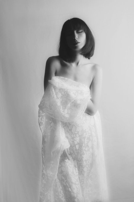 A black and white artistic portrait of a woman with a bob haircut wearing a white lace garment, her eyes closed in a serene pose.