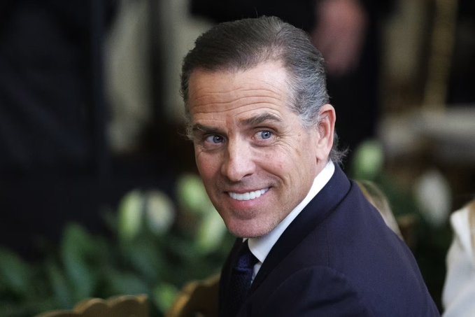 Hunter Biden smiles over his shoulder at an event, accompanying news of his launch of a meme coin called $LAPTOP on the Base blockchain.