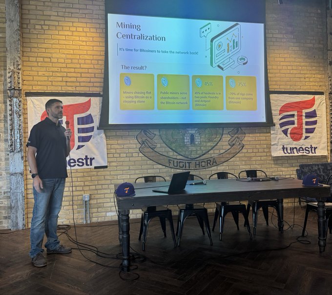 A man stands presenting at a 'tunestr' meetup, speaking into a microphone next to a projected slide titled 'Mining Centralization' discussing Bitcoin miners and pools.