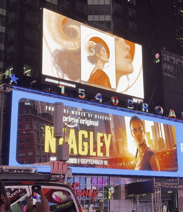 A nighttime photograph of large billboards in Times Square, including one advertising 'THE LORD OF THE RINGS: THE RINGS OF POWER' with artwork signed 'JORGE DESIGNS,' and another promoting 'NAGLEY' with text indicating new episodes on Wednesdays starting September 16.