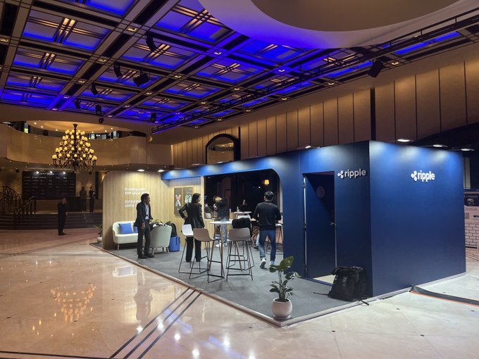 The Ripple-branded booth is set up and ready, with attendees gathered around the counter and lounge area as XRP Seoul 2026 kicks off in the venue's grand hall. The illuminated "ripple" signage on the blue panels confirms the company's presence at the event.