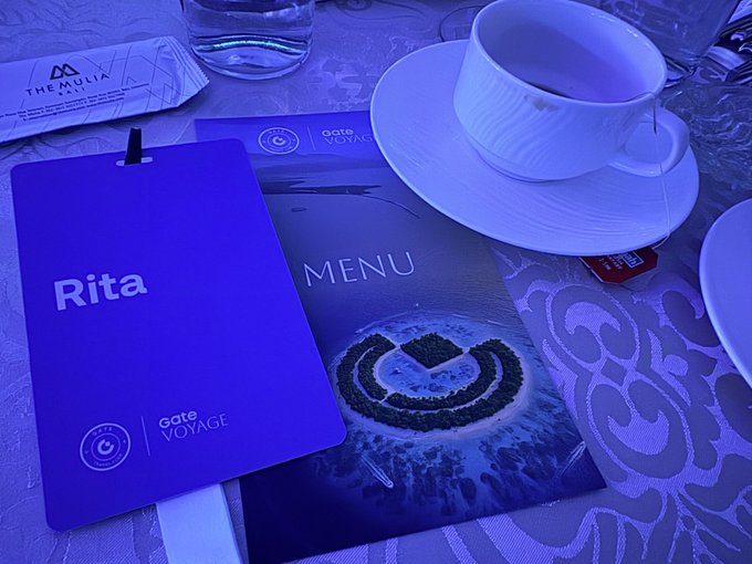 A purple-tinged photo shows a 'Rita' name badge, a menu featuring a 'G' logo, and a white coffee cup on a saucer.