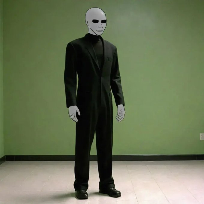 A person stands against a green wall wearing a black suit, black turtleneck, and black shoes, with a blank white mask-like face featuring minimal black facial features.