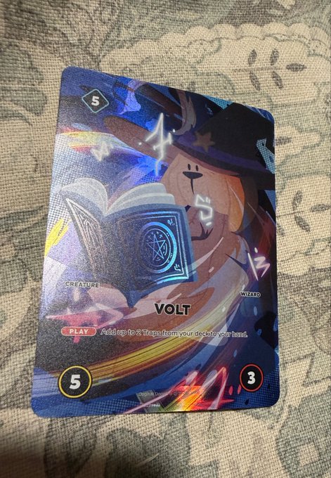 A close-up of a holographic trading card featuring a cartoon character named 'Volt' with stats of 5 and 3, classified as a Creature/Wizard card with the text 'Add up to 2 Traps from your deck to your hand.'
