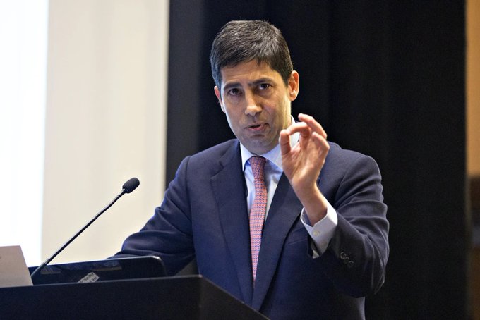 A man in a dark suit and pink tie gestures with his hand while speaking at a podium with a microphone, likely commenting on the upcoming U.S. CPI release mentioned in the post about potential crypto market movements.