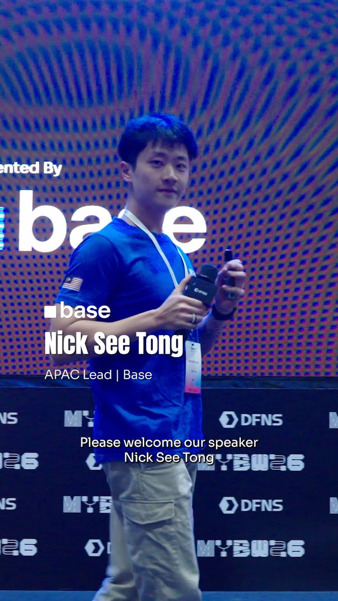 Nick See Tong, APAC Lead at Base, is introduced as a speaker while holding a microphone and water bottle at a conference with sponsor logos including DFNS and MYBWA26.