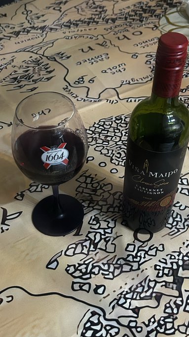 The image features a wine glass filled with red wine, placed next to an unopened bottle of wine. The wine glass has a label that reads "1499", which could be a reference to the year the wine was made or a special edition wine release. The background is a map, and there are some text elements in the image as well. The post seems to be related to a social media platform where people share their thoughts on various topics, including wine.