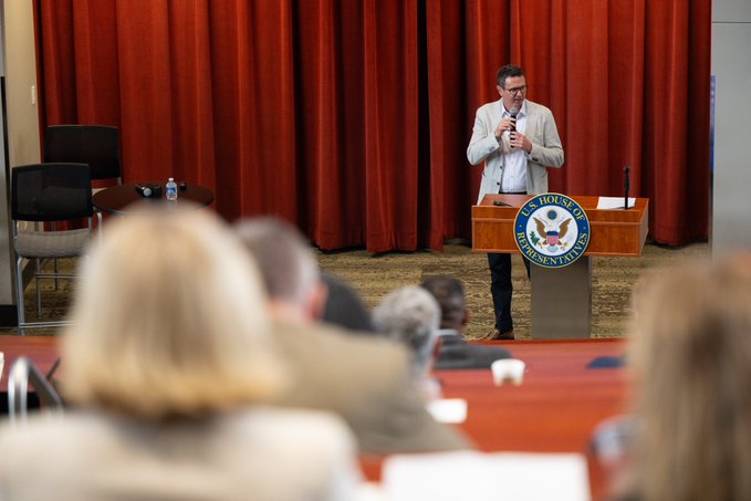 A man with glasses in a light suit jacket speaks into a microphone at a podium displaying the U.S. House Judiciary Committee seal, with an audience seated in the foreground.