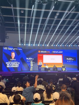 An audience faces a large stage at a Binance-hosted cryptocurrency conference, with screens displaying 'BITCOIN HALVING' and audience voting results of '79,837 SALT'.