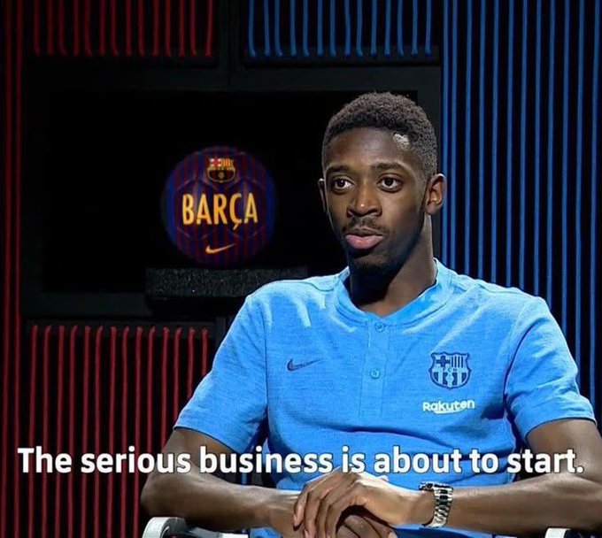 The image features a man wearing a blue shirt sitting down with his hands folded on his lap. The background of the image shows a television screen displaying an advertisement for Barcelona, along with the text "The Serious Business is about to start." This suggests that the man might be discussing or promoting a business idea related to the city of Barcelona.
