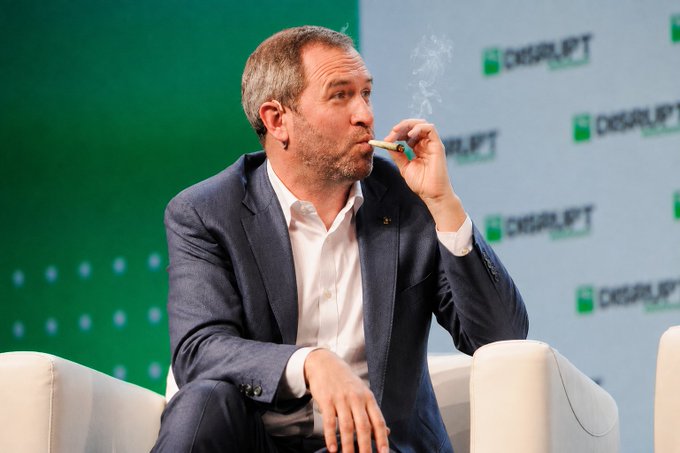 A man in a blue suit jacket and white shirt sits in a chair, smoking a cigar, with a 'CHECKRUPT' logo backdrop behind him.