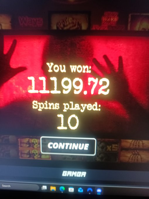 A photograph of a computer monitor displaying a slot machine win screen reading 'You won: 11199.72' with 'Spins played: 10' and a 'CONTINUE' button, with hands raised in excitement against a red background.