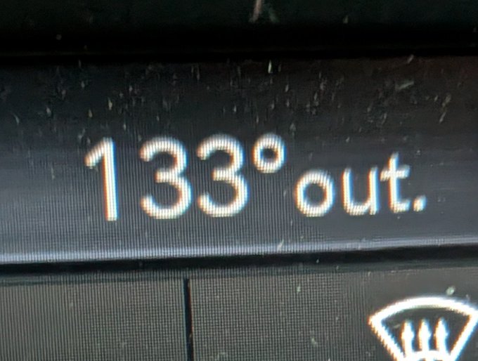 A digital car dashboard display reads "133° out," showing the extreme outside temperature as someone returns to Texas. The image humorously illustrates the post's reference to welcoming the extreme Texas heat.