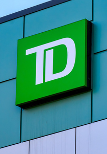 A green square sign with the white "TD" logo is mounted on a teal-colored building facade, representing TD Cowen—the firm that just raised its 2029 Bitcoin price target to $280K, implying 240% upside over three years.