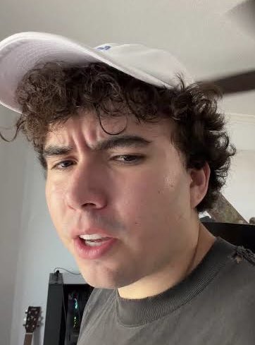 A young man with curly brown hair and a white cap makes a skeptical, squinting face at the camera, appearing unconvinced by the claim that someone gained 40 lbs from the "DUVE memecoin" trading effect.