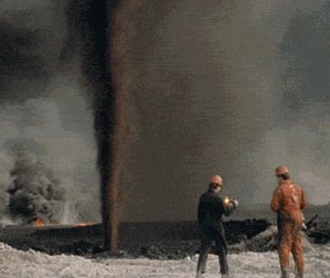 The image shows two men standing near a large black object, which appears to be an oil well or a similar industrial structure. One of the men has a flashlight in his hand, possibly inspecting the equipment or working around the site. The other man is wearing an orange jumpsuit and is holding a camera, likely capturing images or documenting their work at the location. The presence of the oil well suggests that they might be involved in the oil industry, either as workers or as observers.