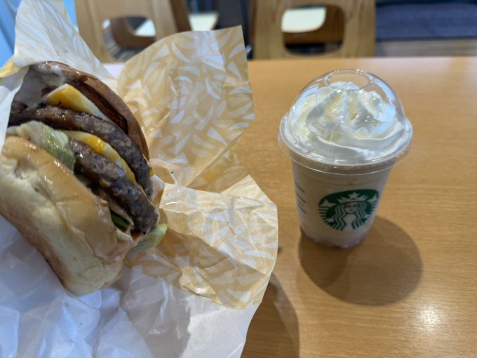 The image features a table with two items, including a burger wrapped in paper and a cup of ice cream or milkshake. The food items are placed next to each other, creating an appealing presentation for potential customers at a restaurant.