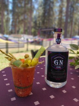 A bottle of GN Gin sitting next to a Bloody Mary cocktail garnished with olives, green peppers, and celery on a table with a purple polka-dot tablecloth.
