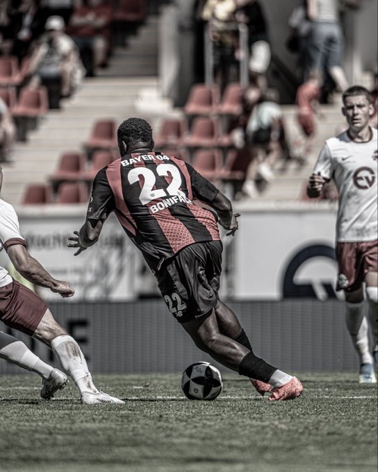 A sports photograph showing a soccer player from Bayer 04, wearing jersey number 23 with 'BONIFACE' on the back, about to kick a ball during a match.