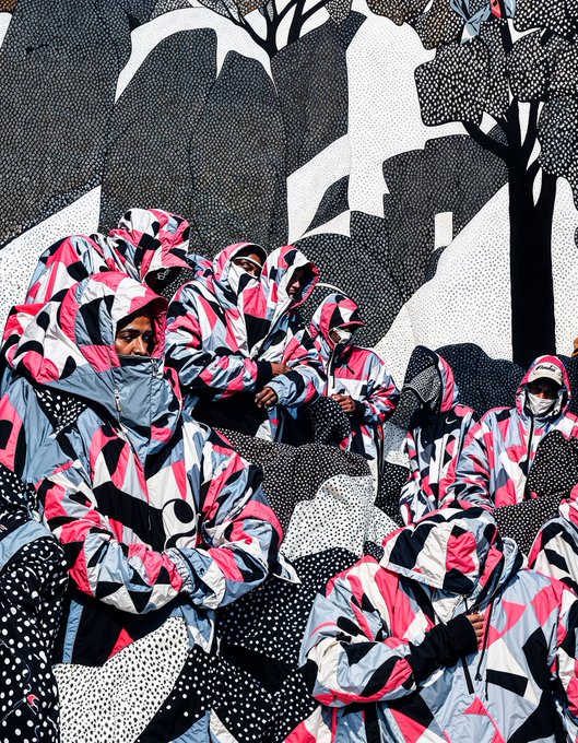 A group of people wearing matching pink, black, white, and grey camouflage hoodies posing in front of a graffiti wall with black and white abstract designs.