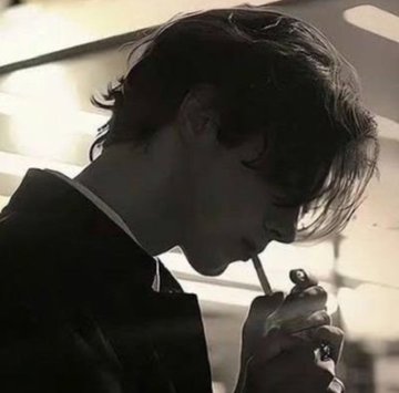A moody, dimly lit close-up shows a young man with dark hair smoking a cigarette, looking downward.