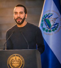Nayib Bukele, President of El Salvador, speaks at a podium bearing the presidential seal, with the Salvadoran flag displayed behind him. The image complements the post celebrating El Salvador's accumulation of 7,746 Bitcoin, valued at nearly $500 million.