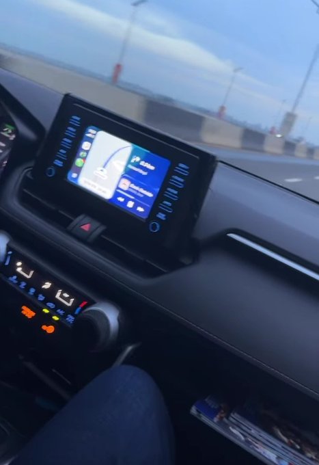 The image shows a person's hand resting on the dashboard of a car, with the car's controls visible beneath their touch. The controls are lit up, indicating that they may be used frequently or in use at the moment. The background features a sky filled with clouds, suggesting it could be an overcast day. In addition to these elements, there is text overlaying part of the image, which provides context about the car's interface and its integration into the digital world through cryptocurrency platforms like Bitcoin Cash.