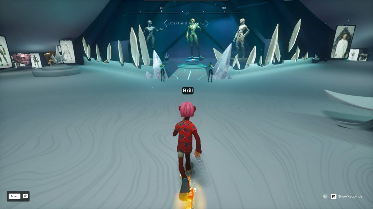The image shows a person wearing a red jacket standing in front of a large screen displaying a video game scene with other players, including a character named "Gri". The player's name appears at the bottom right corner of the screen. The background features a large screen and several people playing the game together.