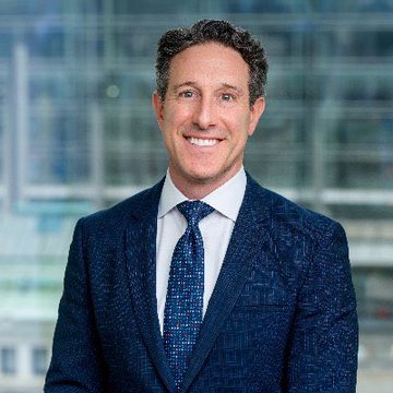 Ryan VanGrack, Vice Chairman at Coinbase, smiles in a professional headshot wearing a navy blue suit and patterned tie, visually accompanying his commentary on the growing momentum behind the CLARITY Act and the increasing pressure for regulatory clarity in the crypto space.