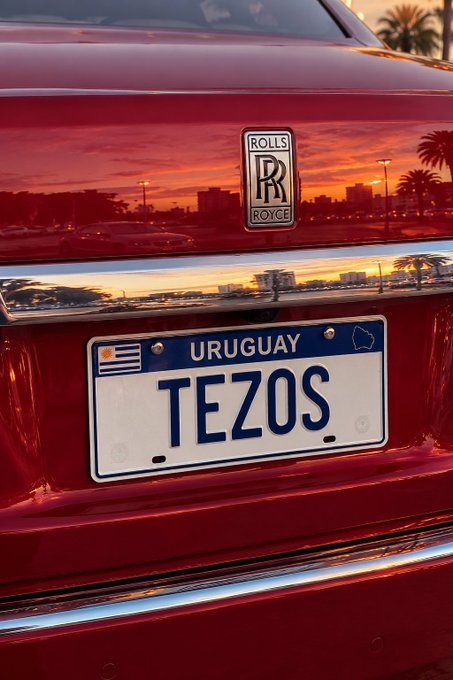 The rear of a red Rolls Royce showing its license plate which reads 'TEZOS' with 'URUGUAY' displayed at the top.