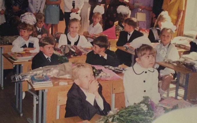 A vintage classroom photo shows young students in formal uniforms seated at wooden desks, some with bouquets and schoolwork in front of them. It evokes the accompanying post’s nostalgia for school days, with the caption suggesting one of the little girls later became involved in crypto; no names, text, numbers, or tickers are visible.