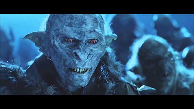 A close-up of a pale blue-skinned creature with pointed ears, sharp teeth, and glowing red eyes in a blue-tinted scene.