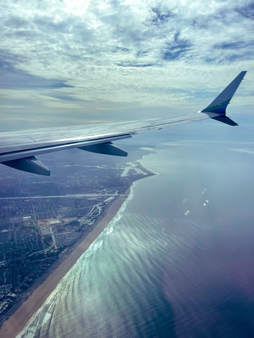 A view from an airplane window showing the wing over a coastline with beach, ocean, and cityscape, capturing the arrival into Los Angeles. The image perfectly complements the post about the apes popping into LA tonight, illustrating the journey to the city from above.